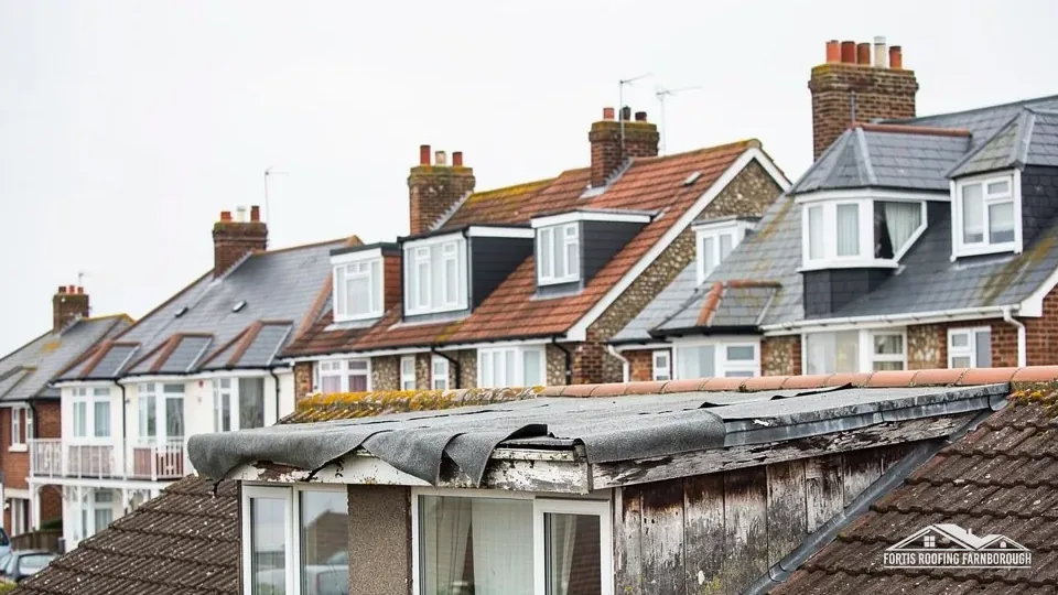 Worn flat roof over a dormer with lifting edge felt, among tiled roofs
